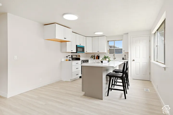 Bright kitchen featuring white cabinetry, a central island with countertop seating, stainless steel appliances, and wood-finish flooring