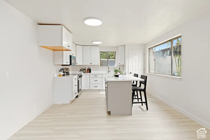 Kitchen featuring white cabinetry, light-toned wood-finish flooring, recessed lighting, and a kitchen island with seating