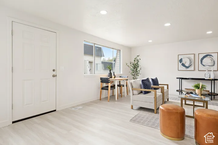 Bright, open living area featuring light wood-finish flooring, recessed ceiling lighting, and large windows with natural light