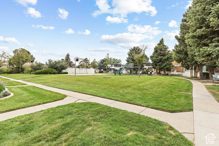 Expansive green space featuring a playground structure, basketball hoop, and concrete pathways