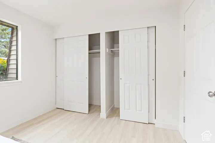 Double bi-fold closet doors with storage rods, wood-finish flooring, and a single window
