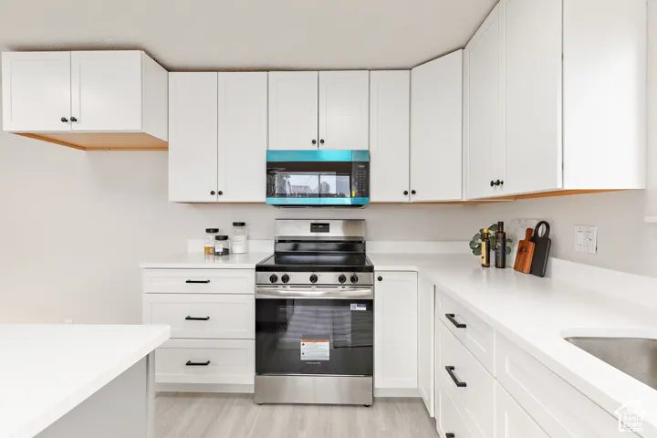 White shaker-style cabinetry with matte black hardware, stainless steel range, built-in microwave, and light-toned countertops
