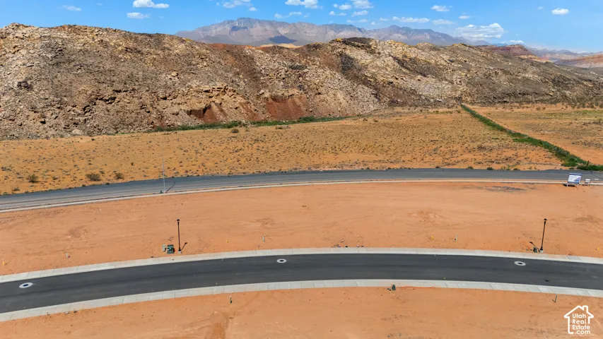 Curved asphalt roadway with concrete curb and gutter, bordered by undeveloped desert landscape and distant mountains