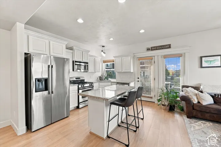 White shaker-style cabinetry, stainless steel appliances, light wood-finish flooring, recessed lighting, and a kitchen island with seating