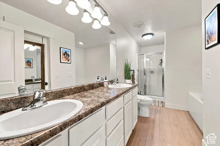 Dual basin vanity with integrated white sinks, wood-finish flooring, and a glass-enclosed shower