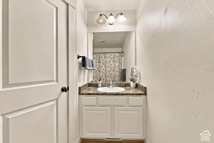 White paneled door, single vanity with light-toned countertop, white under-mount sink, three-light vanity fixture, and wall-mounted mirror
