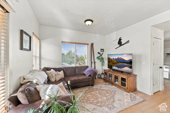 Bright living area featuring wood-finish flooring, white walls, and multiple windows with blinds