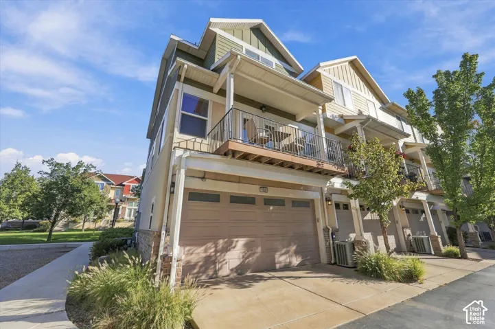 Multi-level townhome exterior featuring an attached two-car garage, stone veneer accents, and private balcony with metal railing