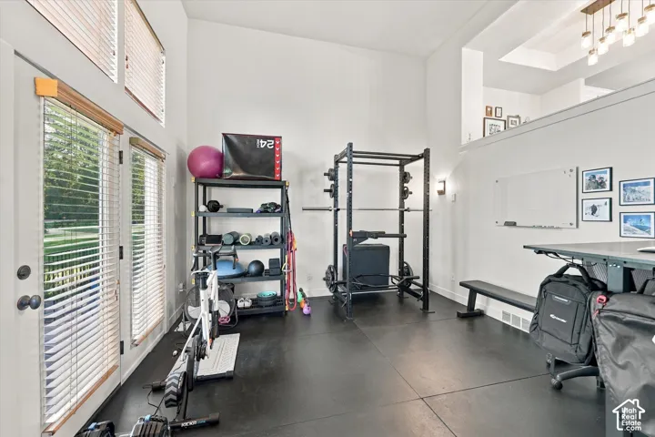High ceilings, dual French doors with integrated blinds, rubberized flooring, and a recessed ceiling feature with a chandelier
