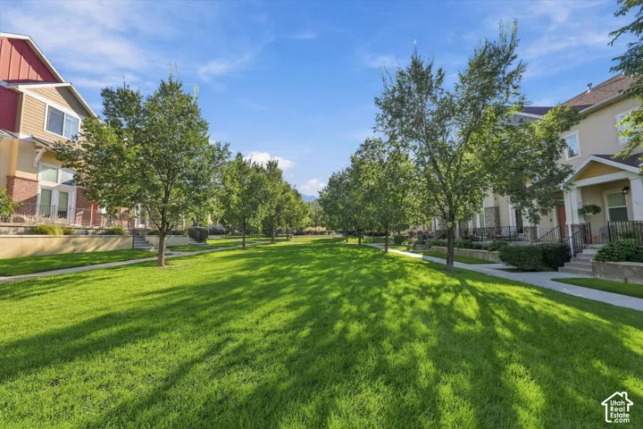Expansive green space bordered by mature trees and paved walkways, featuring multi-story residences with varied exterior finishes including brick and siding