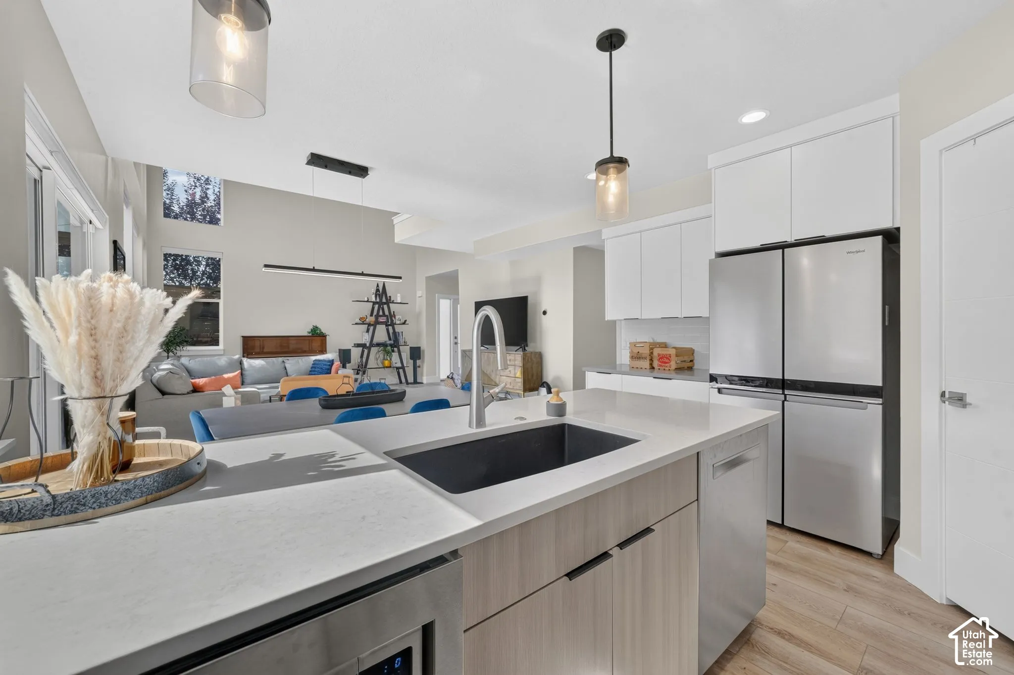 Kitchen island with an undermount sink, contemporary pendant lighting, and light-toned cabinetry