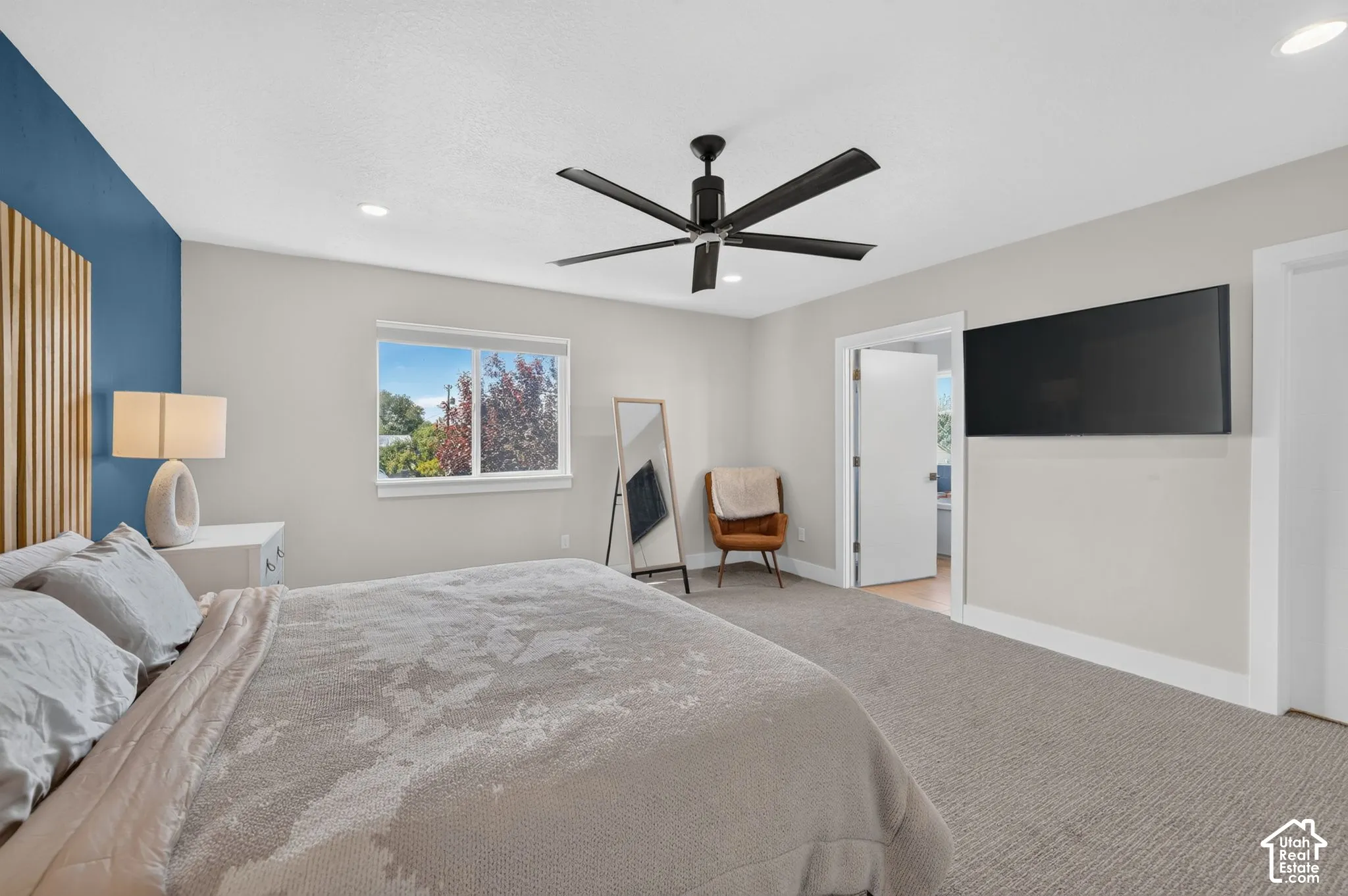 Recessed lighting, ceiling fan with black finish, light gray carpeting, window with outdoor scenery, and a blue accent wall with wood paneling