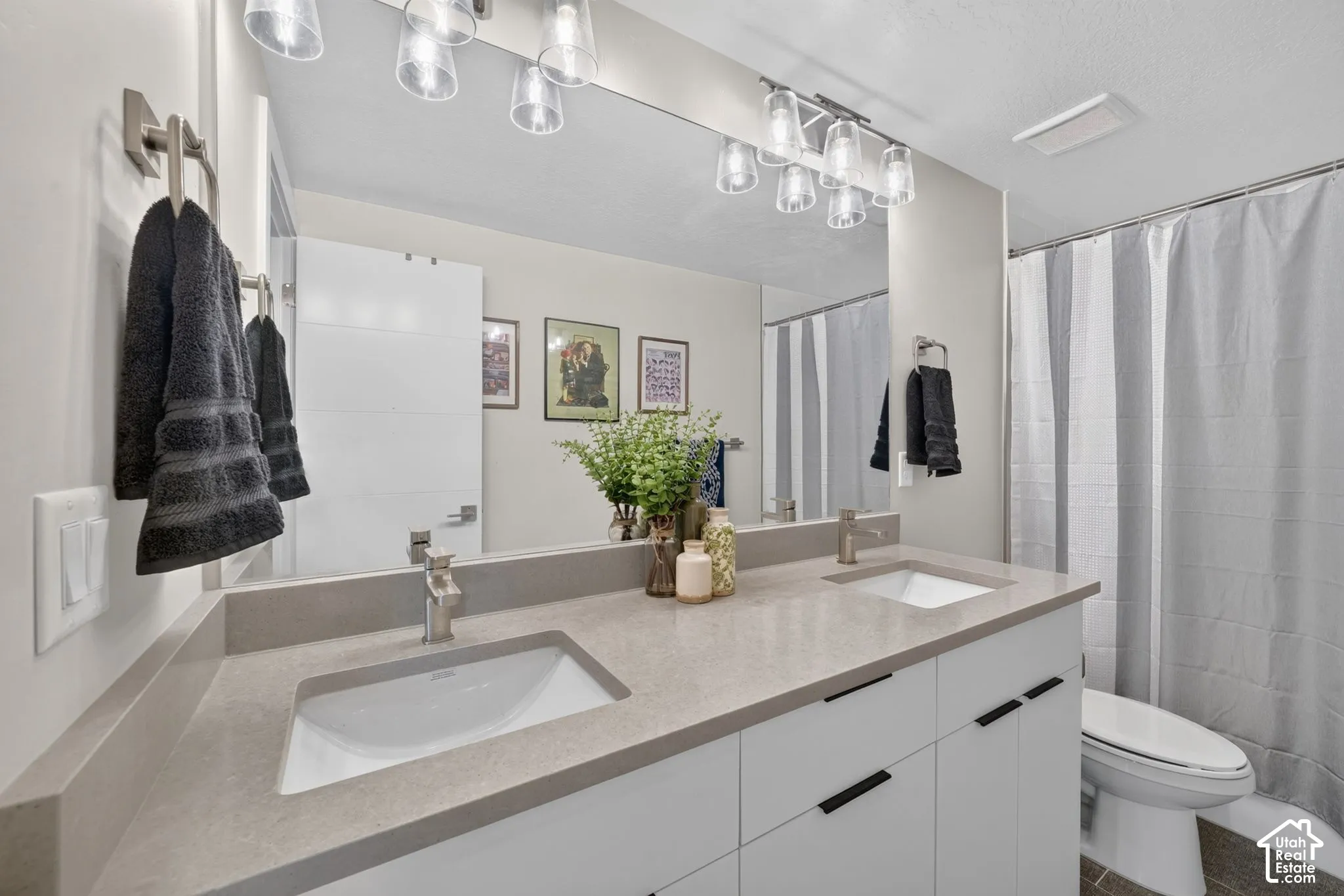 Second full bathroom with double vanity with integrated sinks, extensive mirror, modern light fixtures, and under-cabinet storage