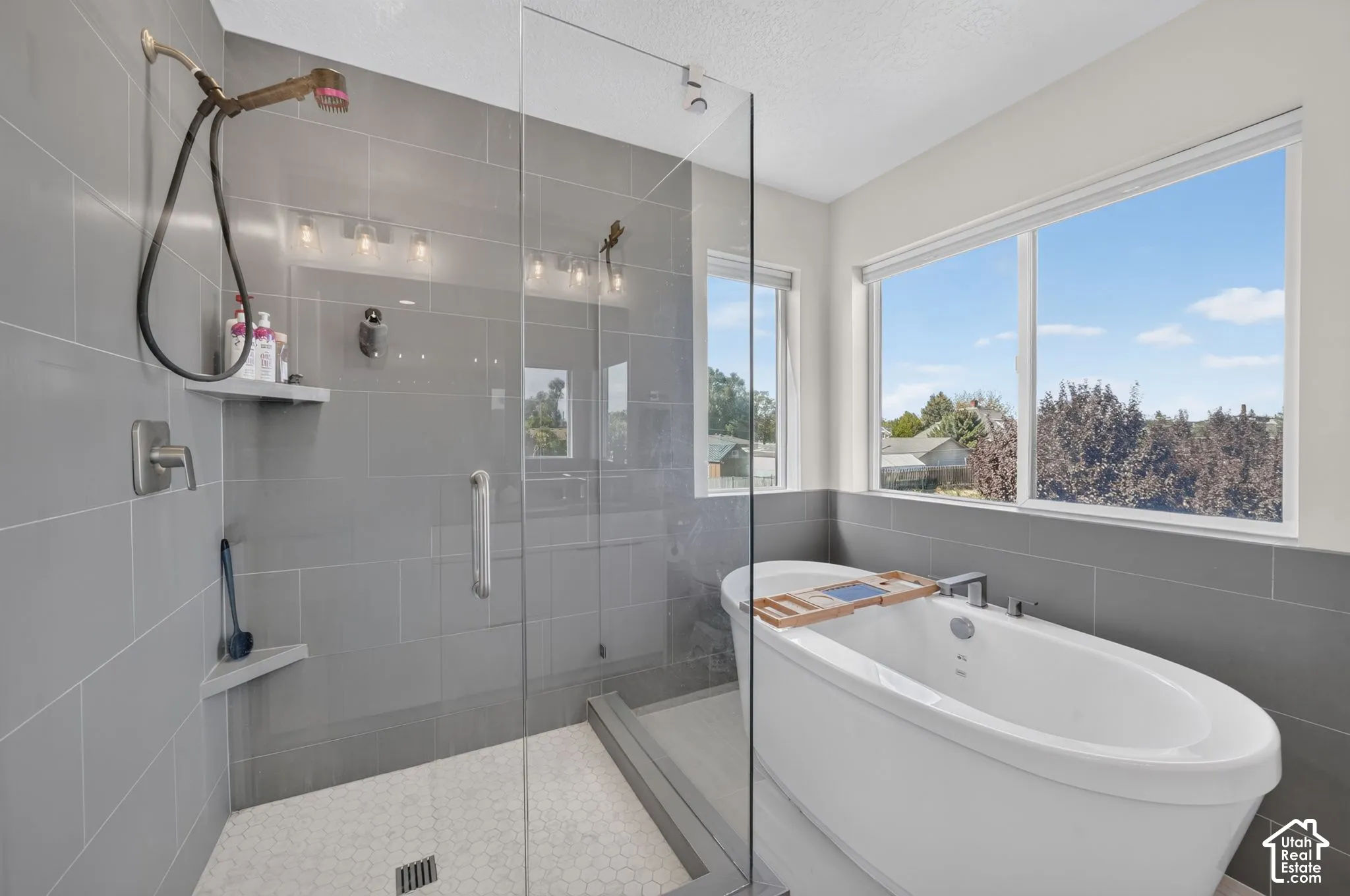 Walk-in shower with tiled walls and hex tile flooring, freestanding soaking tub, and large north-west facing windows