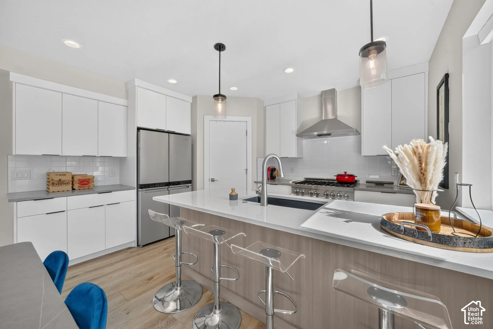 Modern kitchen featuring stainless steel appliances, white cabinetry, a large island with an integrated sink, recessed lighting, and wood-finish flooring