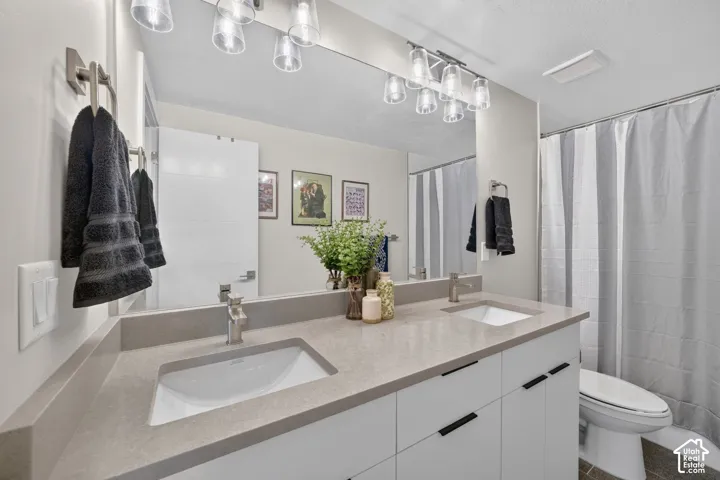 Second full bathroom with double vanity with integrated sinks, extensive mirror, modern light fixtures, and under-cabinet storage