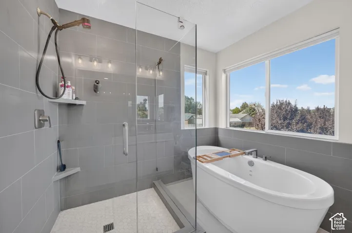 Walk-in shower with tiled walls and hex tile flooring, freestanding soaking tub, and large north-west facing windows