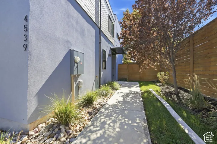 Concrete walkway with landscaped rock and grass borders, complemented by a horizontal slat wood fence