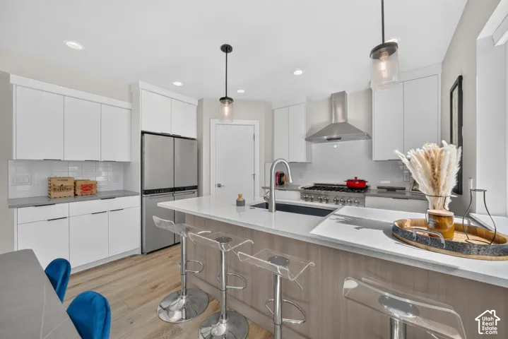 Modern kitchen featuring stainless steel appliances, white cabinetry, a large island with an integrated sink, recessed lighting, and wood-finish flooring