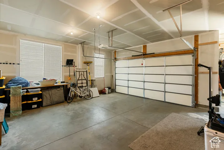 Attached garage with a concrete floor, two windows featuring horizontal blinds, and a white sectional garage door