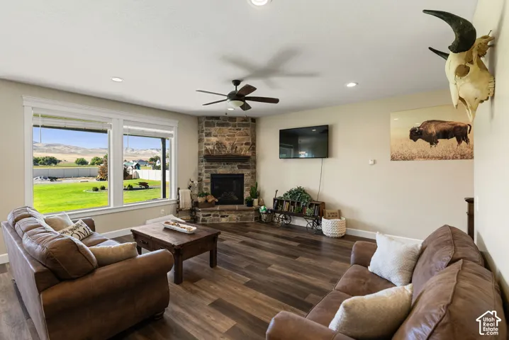 Spacious living area featuring wood-finish flooring, a corner stone fireplace with a wood mantle, and a ceiling fan