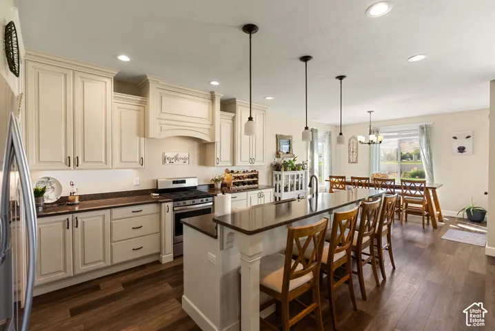 Kitchen featuring cream-colored cabinetry, stainless steel range, a large island with seating, and wood-finish flooring