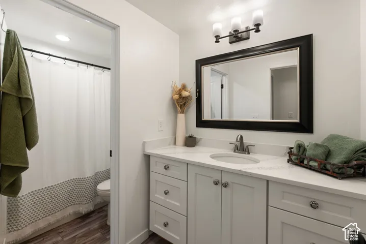 White shaker cabinetry with decorative hardware, quartz-finish countertop, single basin sink with brushed nickel faucet, large framed vanity mirror, and wood-finish flooring