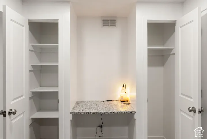 Built-in desk nook with a stone-finish countertop, flanked by two storage closets with built-in shelving and panel doors