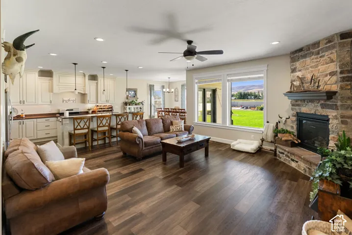 Open concept living area featuring wood-finish flooring, a stone-clad fireplace, and a kitchen with light-colored cabinetry and an island