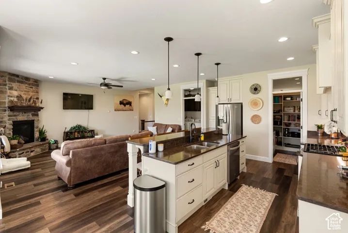 Open-concept living space featuring wood-finish flooring, a stone fireplace, and a kitchen island with pendant lighting