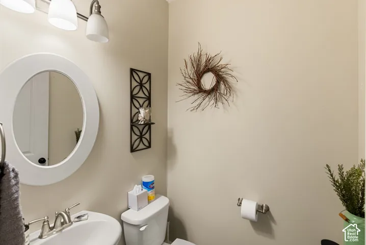White oval mirror, pedestal sink with chrome faucet, and overhead vanity lighting