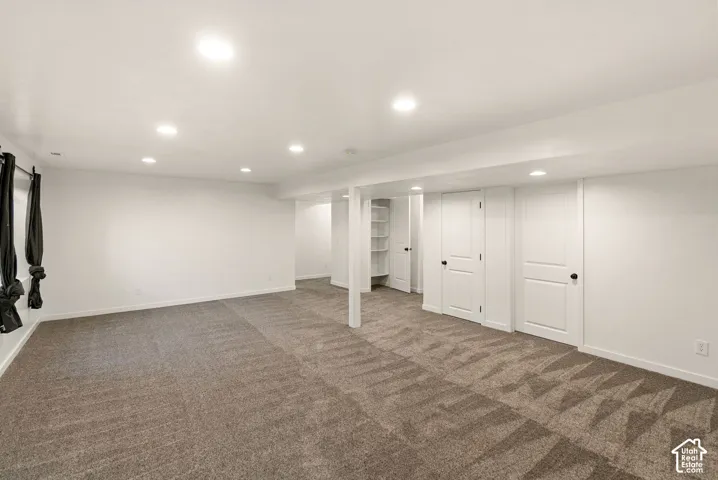 Spacious room with recessed lighting, light-colored walls, patterned carpet, white doors with black hardware, and built-in shelving