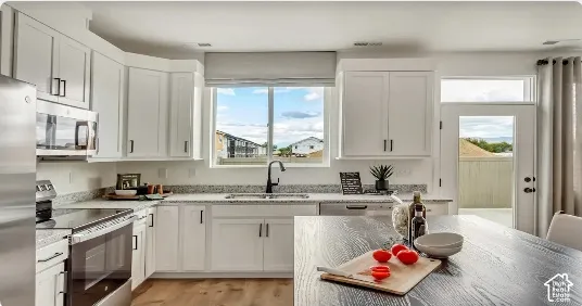 Modern kitchen featuring white cabinetry, stainless steel appliances, light-toned countertops, and wood-finish floorings. This home is under construction. Pictures are of a similar home