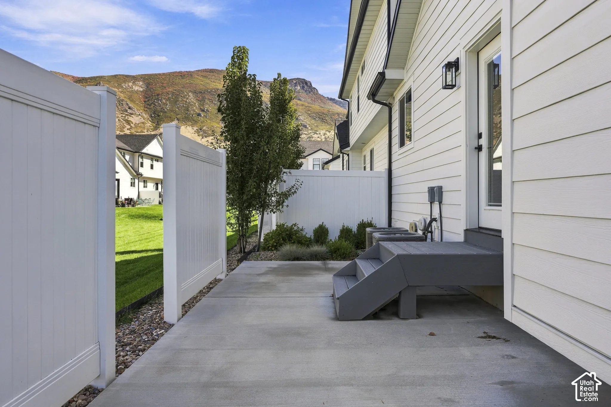 White siding exterior with a concrete patio, dark gray steps, and a white fence