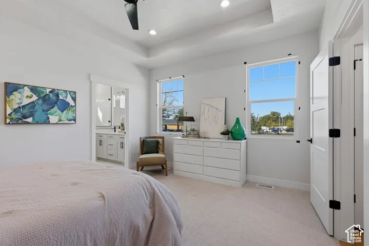 Main level primary suite with tray ceiling, ample natural light, neutral colors and attached bath