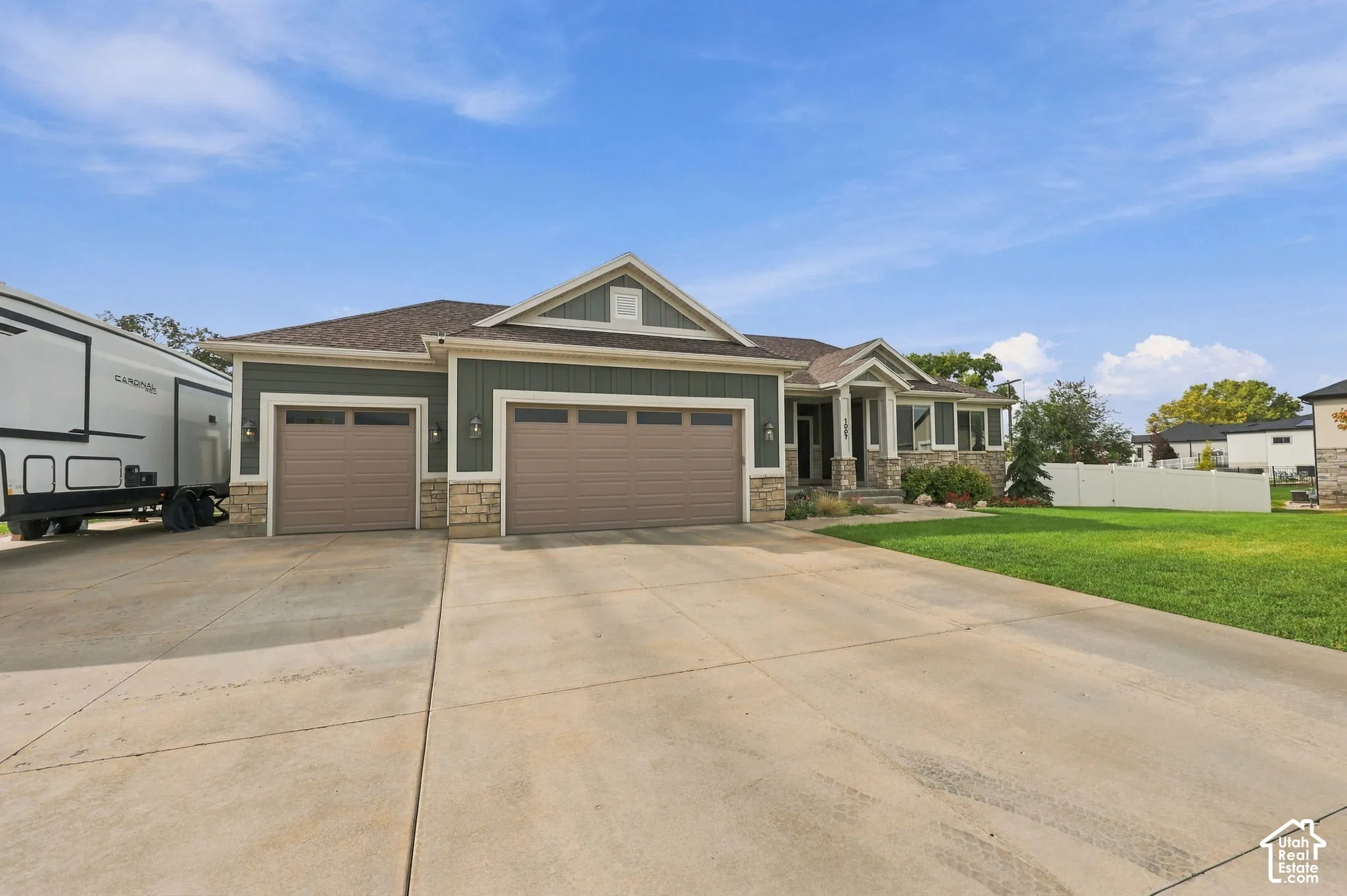 Exterior featuring green siding, stone accents, a multi-car garage, and a concrete driveway