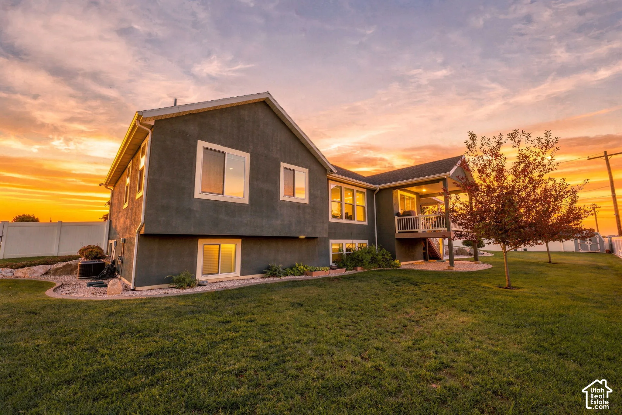 Exterior featuring a covered balcony, lower-level patio, multiple windows, and a fenced perimeter