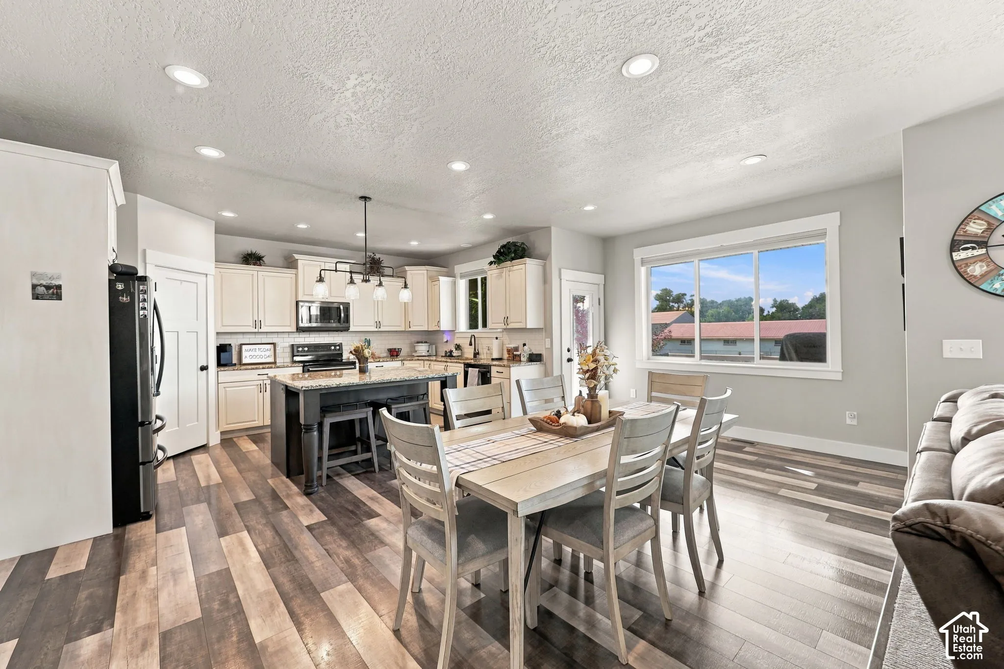 Open-concept living space with wood-finish flooring, recessed lighting, and a well-appointed kitchen featuring light-colored cabinetry, a center island with seating, and stainless steel appliances
