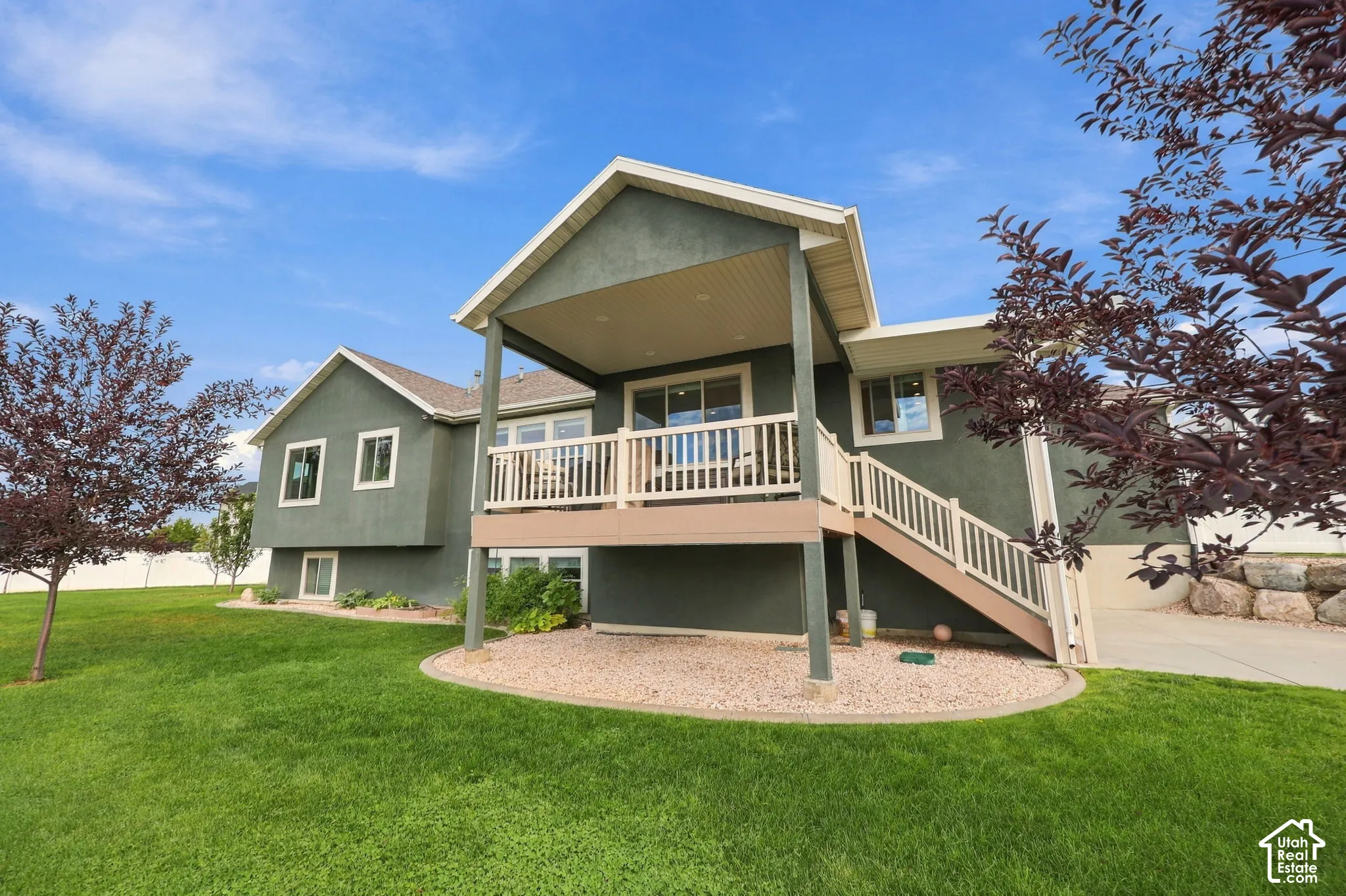 Rear exterior featuring a covered deck with white railing, exterior stairs with white railing, and a lower-level concrete patio