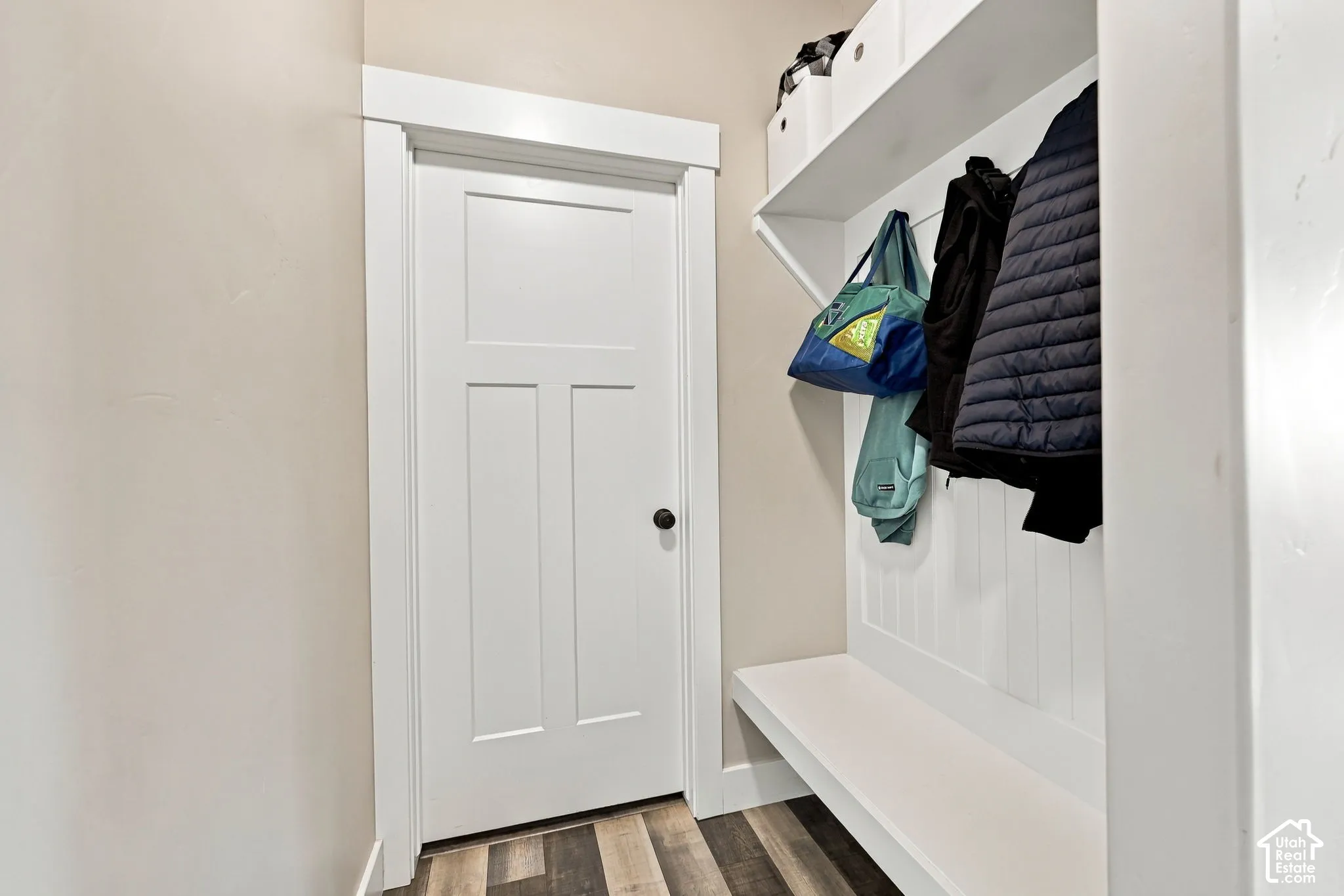 Entryway featuring a built-in bench, overhead shelving, wall-mounted coat hooks, and wood-finish flooring