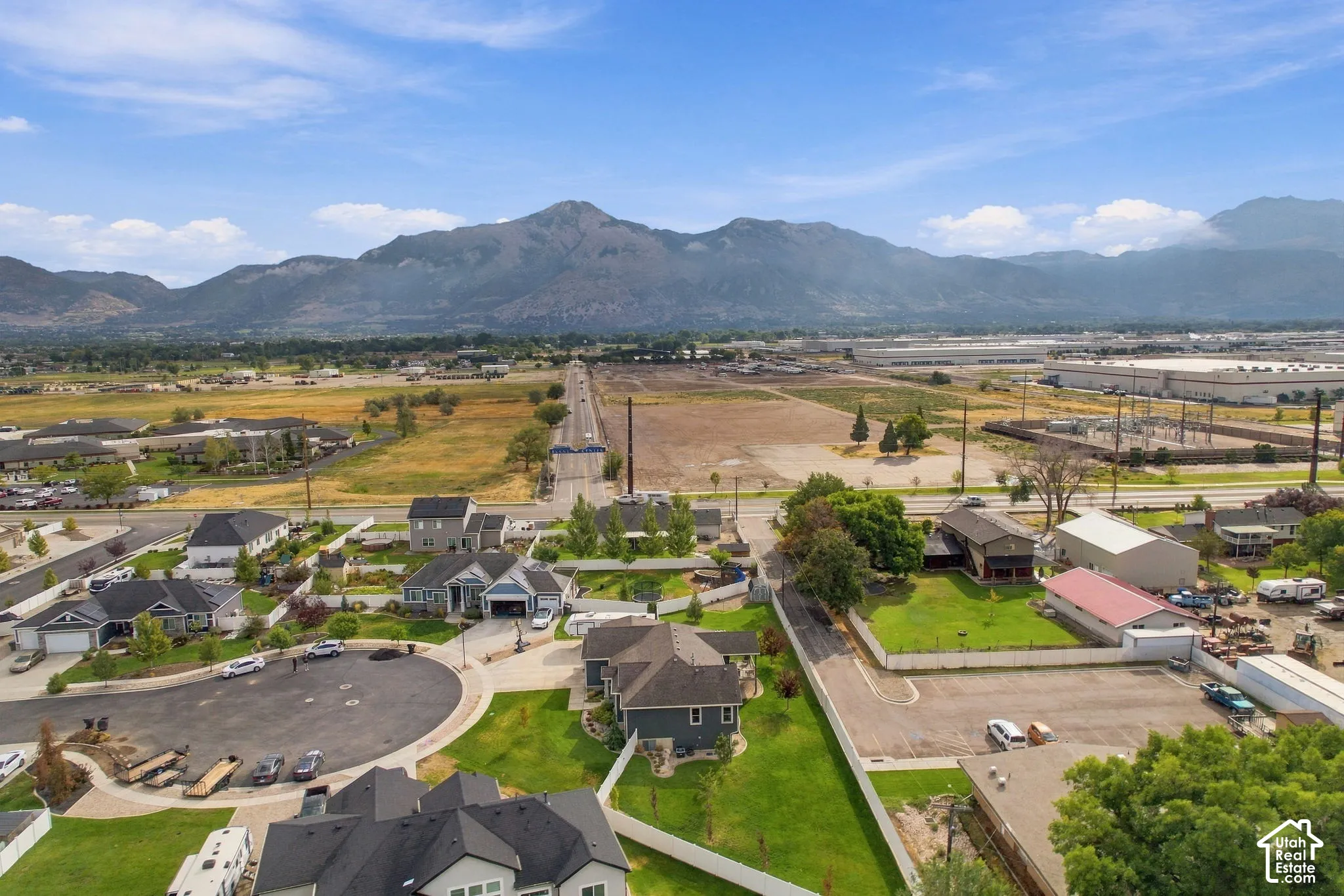 Expansive mountainous backdrop, residential area with established homes, cul-de-sac street design, broad open land, and distant commercial structures