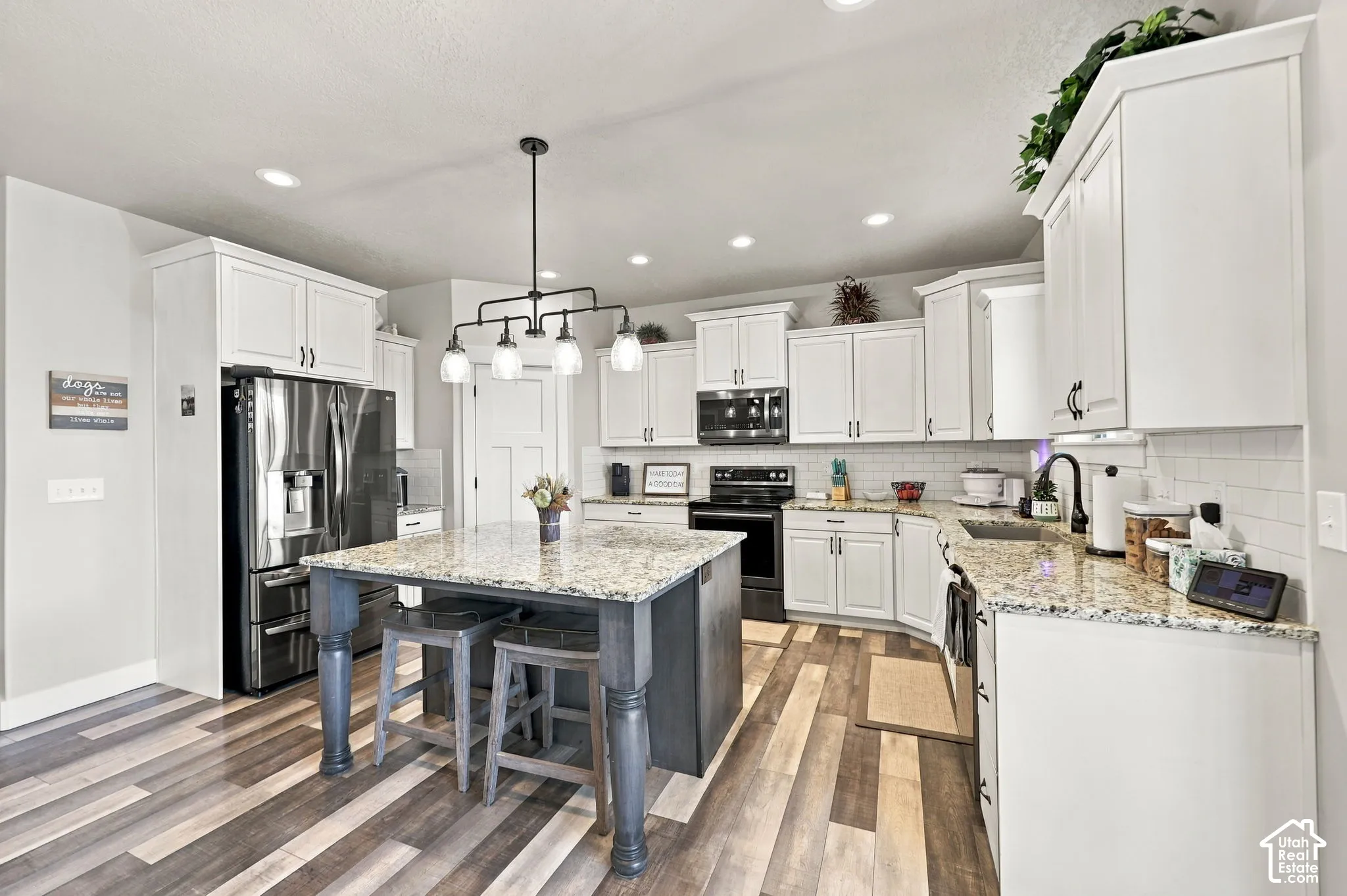 Kitchen featuring white cabinetry, wood-finish flooring, a central island with seating, a stainless steel refrigerator, and granite countertops