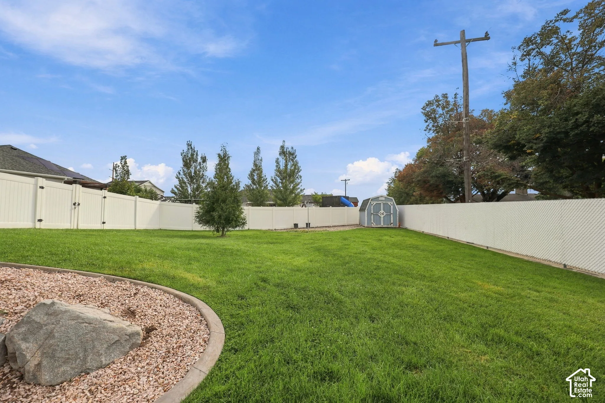 Expansive backyard featuring a manicured lawn, a gravel bed with a decorative boulder, and a white privacy fence