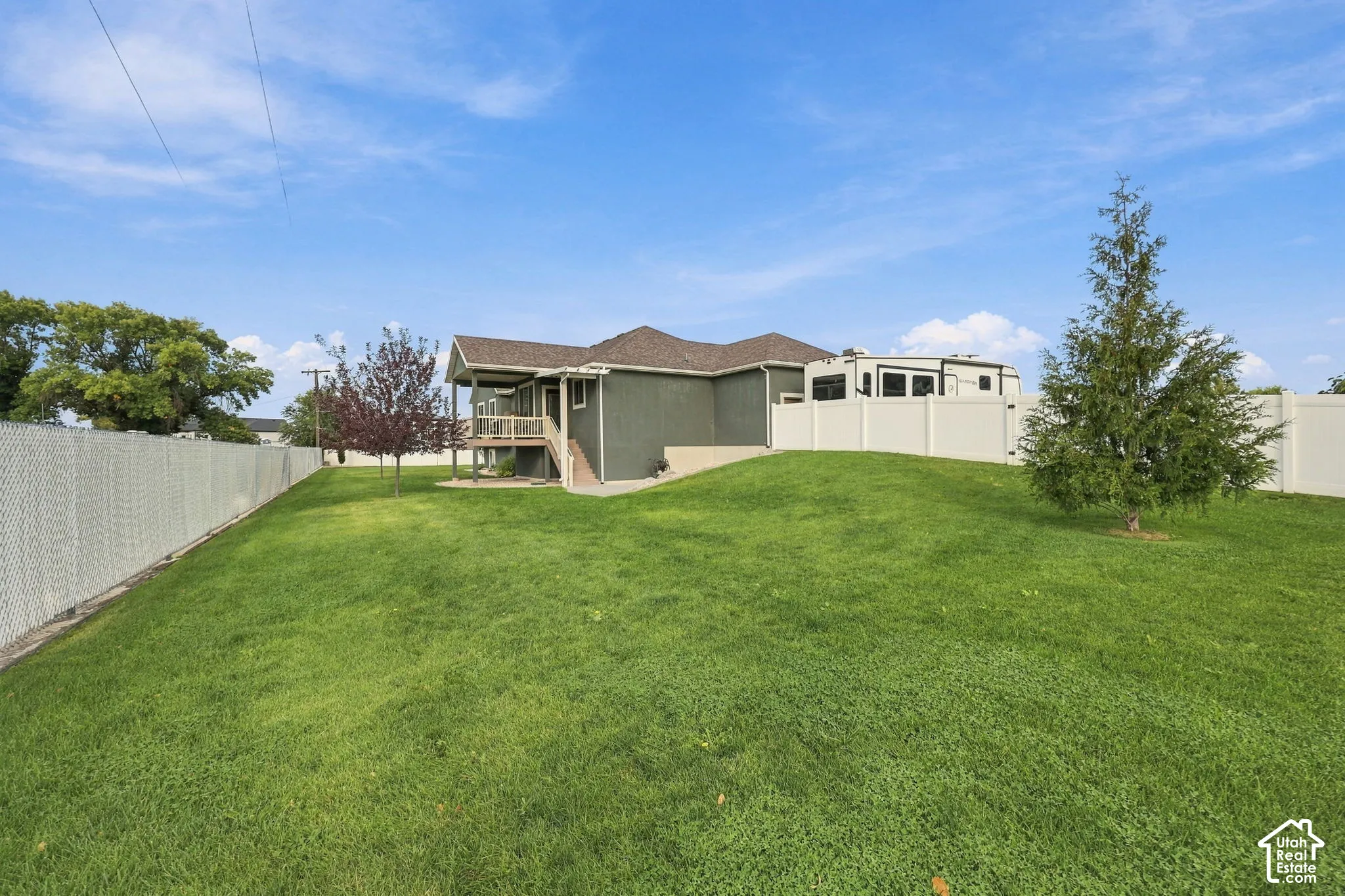 Expansive green lawn with a sloped grade, featuring perimeter chain-link and privacy fencing