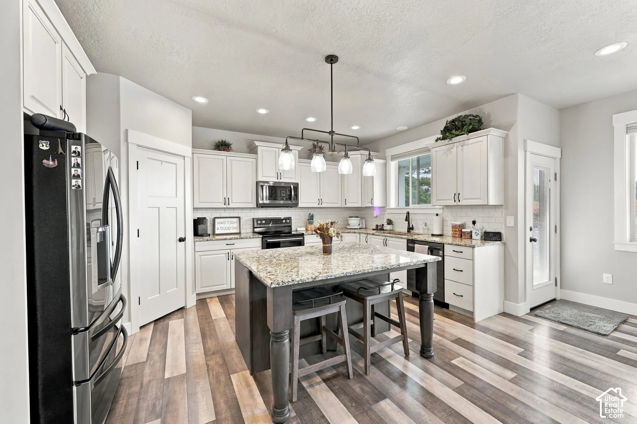 Gourmet kitchen with wood-finish flooring, white cabinetry, a large center island with a granite countertop, pendant lighting, and recessed lighting