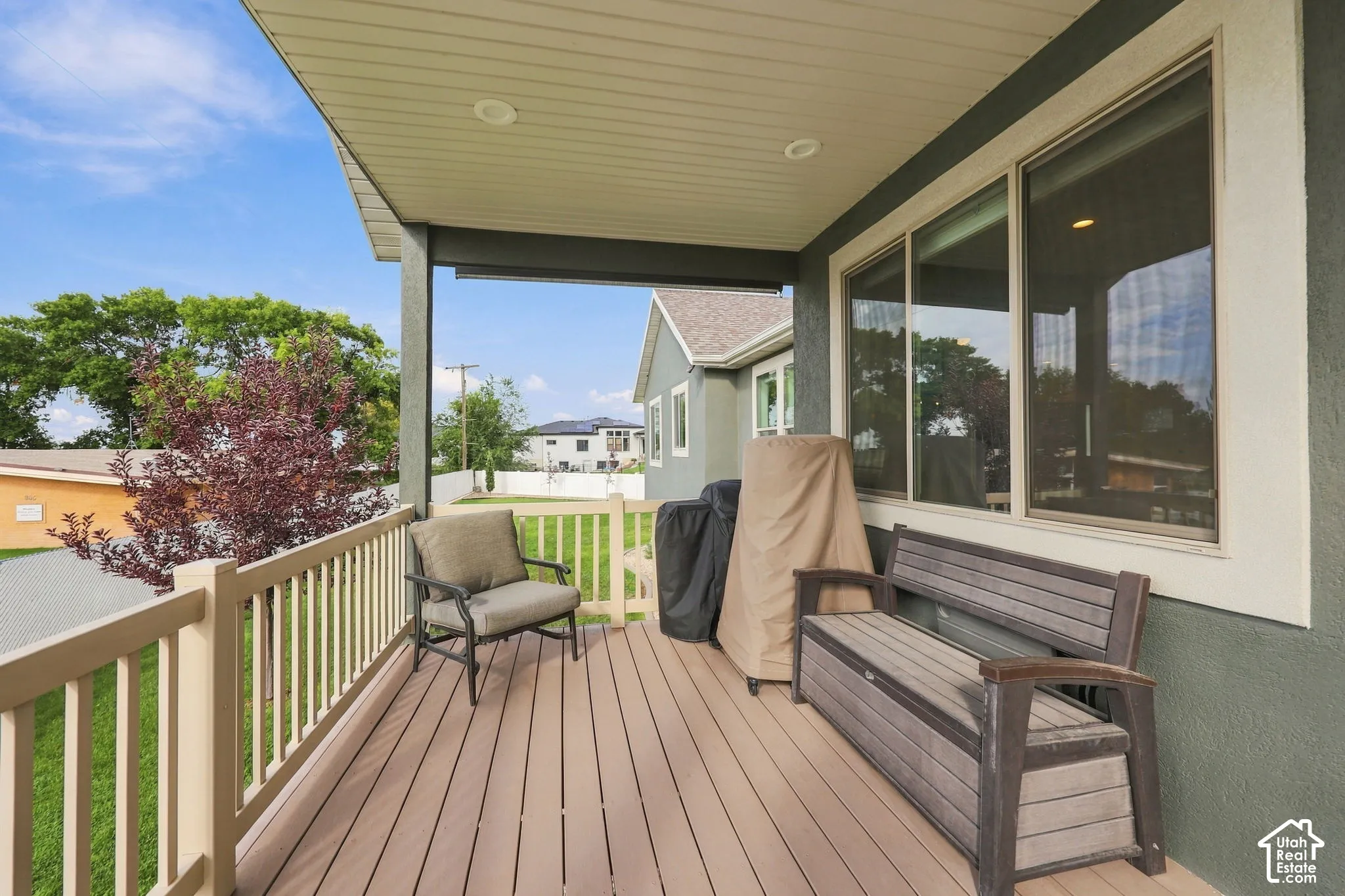 Covered outdoor deck with wood-finish decking, light-toned railing, and a stucco exterior wall