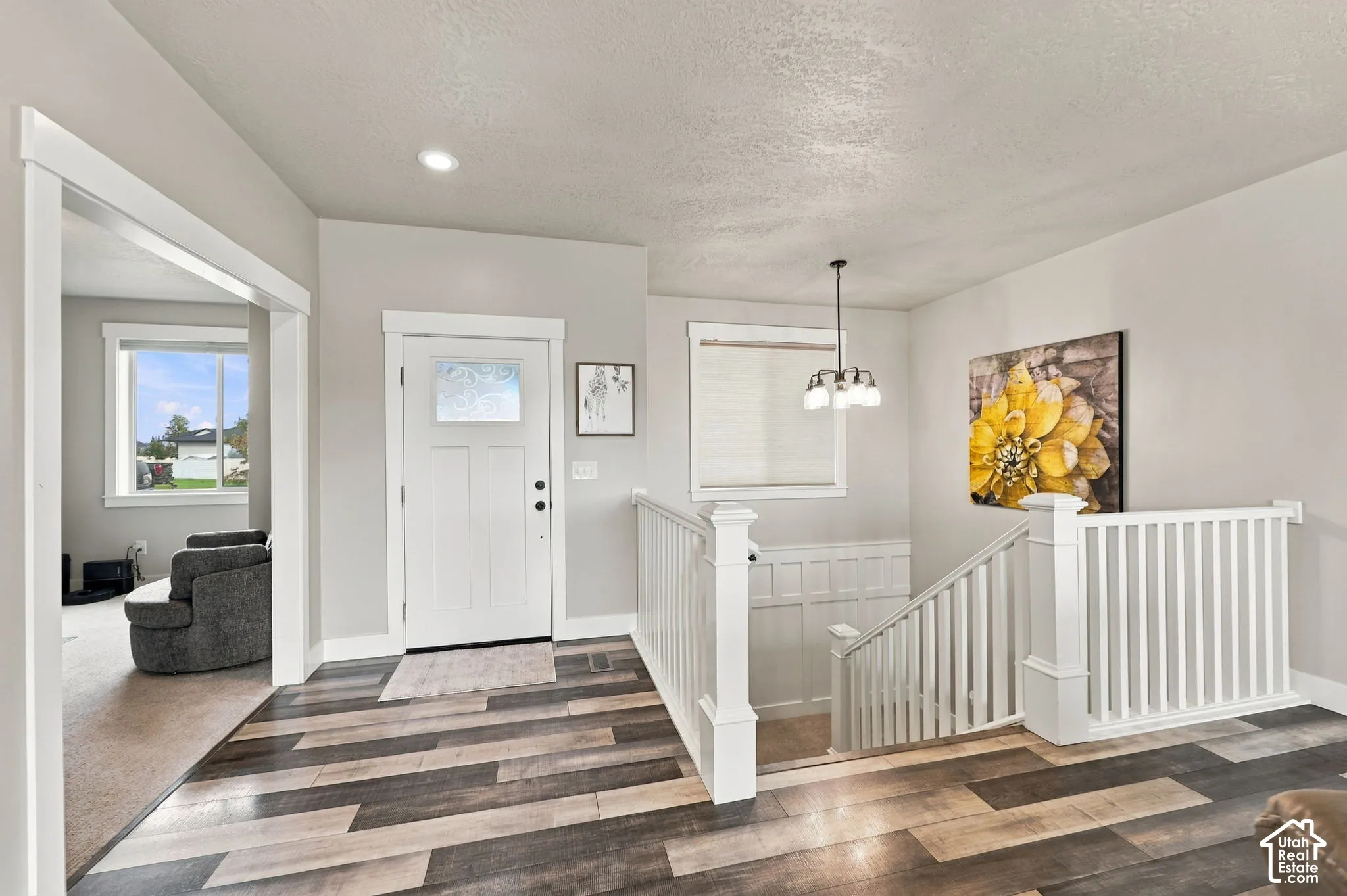 Wood-finish flooring, white paneled entry door with frosted glass, white stair railing with paneled accents, and a contemporary chandelier