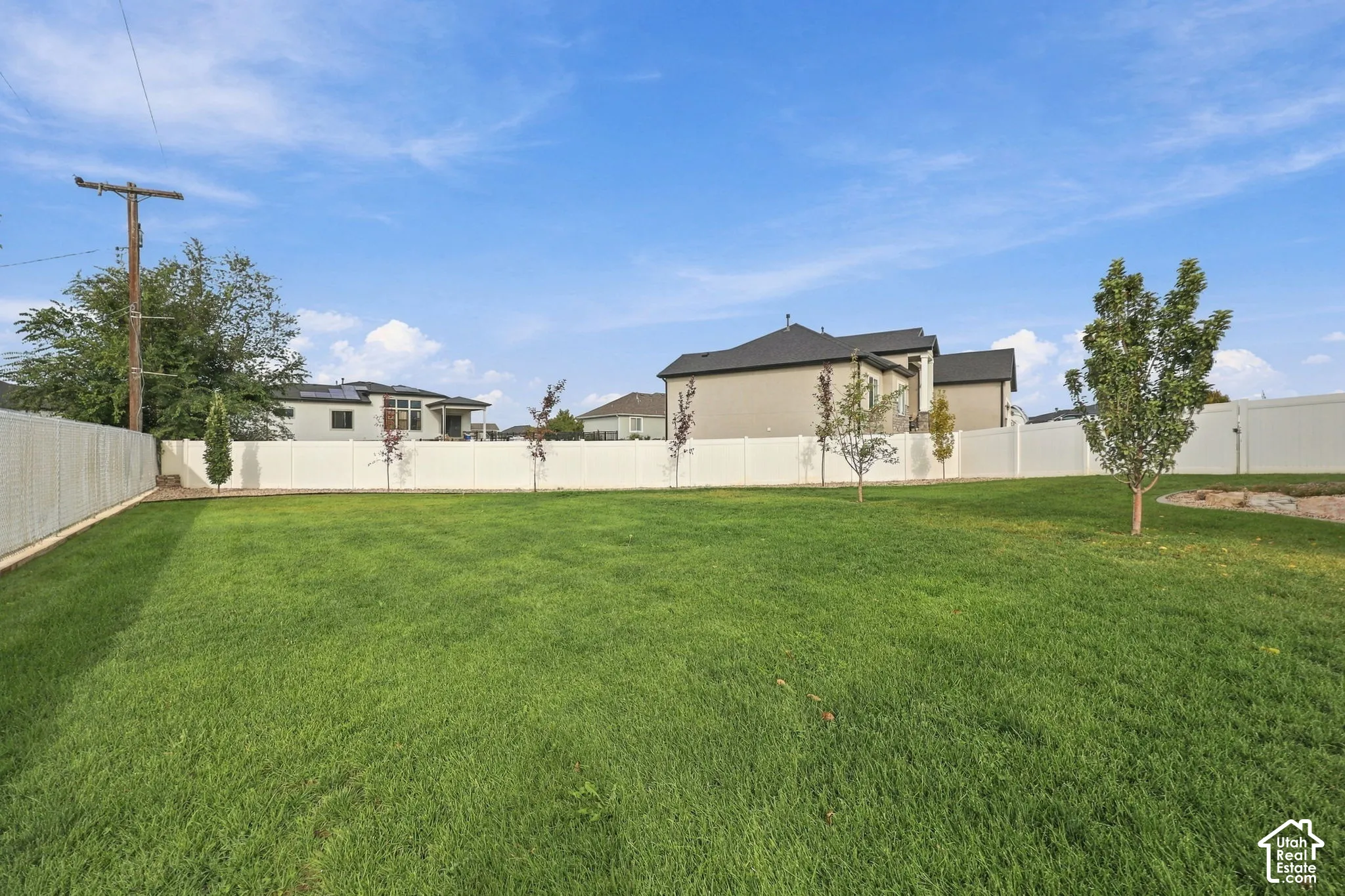 Expansive grass lawn with a full perimeter fence and scattered young trees
