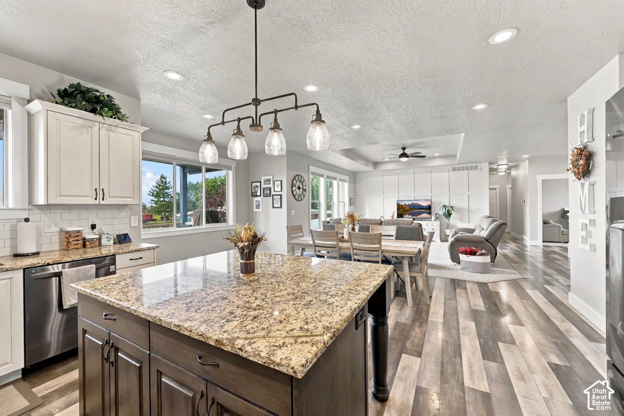 Kitchen island with stone countertop, wood-finish flooring, white cabinetry, stainless steel appliances, and a linear chandelier