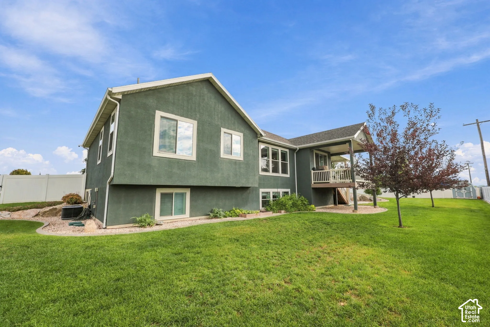 Stucco exterior with white trim, covered deck with white railings, multiple windows, and a landscaped yard